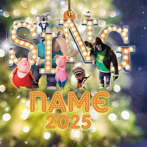May include: A festive ornament featuring the word "SING" in illuminated letters, surrounded by animated characters. Below, the text "NAME 2025" is displayed in a similar style, set against a blurred background of lights.