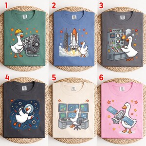 May include: A collection of six t-shirts featuring cartoon geese in various occupations. Designs include a goose mechanic, a space shuttle launch, a reactor operator with text 'REACTOR 1', an astronaut goose, a computer technician, and a satellite operator.
