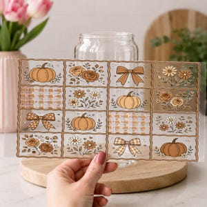 May include: A clear glass tumbler wrap featuring a grid of sixteen rectangular panels. The designs include brown pumpkins, floral arrangements with roses and daisies, tan gingham patterns, and bows in various brown and white color schemes.