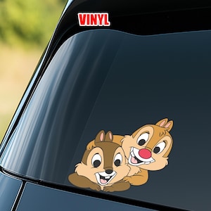 May include: A vinyl sticker featuring Chip and Dale, the cartoon chipmunks, in a friendly embrace. The sticker is in shades of brown, tan, and white, with a red text that reads "VINYL" at the top.