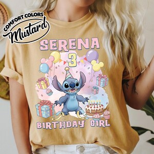 Peut inclure: Un t-shirt jaune moutarde avec une illustration du personnage Stitch portant un chapeau de f&ecirc;te, entour&eacute; de ballons, cadeaux, cupcakes et un g&acirc;teau d'anniversaire. Le texte indique SERENA 3 BIRTHDAY GIRL. Une &eacute;tiquette Comfort Colors Mustard est visible.