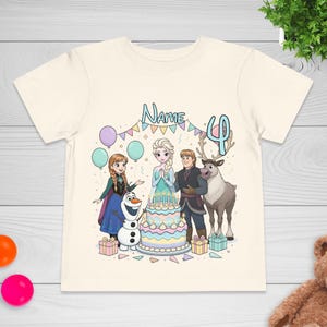 May include: Cream-colored t-shirt featuring a colorful graphic of characters from the movie Frozen, including Elsa, Anna, Olaf, Kristoff, and Sven. The design includes a birthday cake, balloons, and the number 4. The word "Name" is also visible.