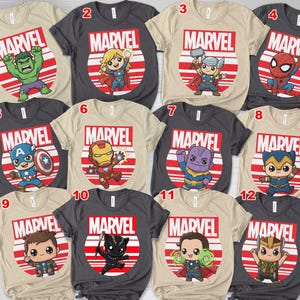 Op de afbeelding: Een verzameling Marvel-thema T-shirts. Elk shirt heeft een andere Marvel-personage-afbeelding in een rood en wit cirkelvormig ontwerp, met het Marvel-logo erboven. De shirts zijn in verschillende kleuren, waaronder beige, grijs en zwart.