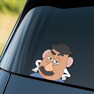 May include: A car window sticker depicting a cartoon character with a brown head, a black hat, and a large black moustache. The character has a neutral expression and is wearing a blue shirt. The sticker is on a car window.