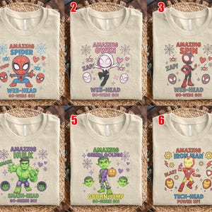 May include: Six beige t-shirts with superhero designs. Each shirt features a different character: Spider-Man, Spider-Gwen, Spider-Man (Miles Morales), Hulk, Green Goblin, and Iron Man. Each design includes the character's name and related phrases.
