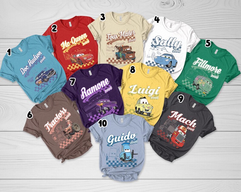 May include: A collection of ten short-sleeved t-shirts in various colors, each featuring a character from the movie Cars with their name, the year 2006, and a checkered flag graphic. The shirts are numbered one through ten and display characters including Doc Hudson, Mc Queen, Tow Mater, Sally, Fillmore, Tractors, Ramone, Luigi, Mach, and Guido.