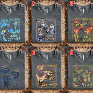 Pode incluir: Seis camisetas cinzentas com diferentes designs de personagens do filme "Zootia 2". Cada camisa apresenta um personagem ou grupo diferente, incluindo Gary De Snake, Judy Hopps, Nick Wilde, Chief Bogo, Finnick e Flash.