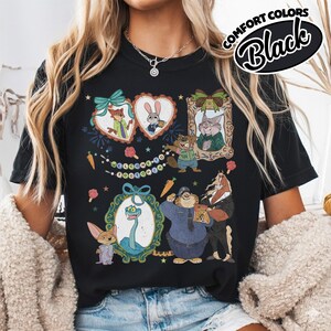 May include: A black t-shirt featuring a graphic print of various Zootopia characters, including Nick Wilde, Judy Hopps, and others, arranged in frames and alongside the text Welcome to Zootopia, with small carrot and popsicle illustrations.