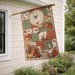 Pu&ograve; includere: Una bandiera da giardino rettangolare con un design patchwork a tema autunnale. La bandiera mostra illustrazioni di oche bianche con fiocchi verdi, zucche arancioni e verdi, ghiande e foglie autunnali nei toni del marrone, dell'arancione e del verde.