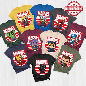 Pode incluir: Uma cole&ccedil;&atilde;o de camisetas com tema Marvel em v&aacute;rias cores, cada uma com um personagem de super-her&oacute;i diferente. As camisetas t&ecirc;m um design circular vermelho e branco com o logotipo da Marvel. Um adesivo "Bulk Discount" &eacute; vis&iacute;vel.