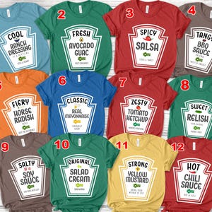 May include: A collection of twelve short-sleeved t-shirts in various colors, each featuring a graphic design shaped like a condiment bottle label. The prints include text such as Cool Ranch Dressing, Fresh Avocado Guac, Spicy Salsa, Tangy BBQ Sauce, Fiery Horse Radish, Classic Real Mayonnaise, Zesty Tomato Ketchup, Sweet Relish, Salty Soy Sauce, Original Salad Cream, Strong Yellow Mustard, and Hot Chili Sauce.