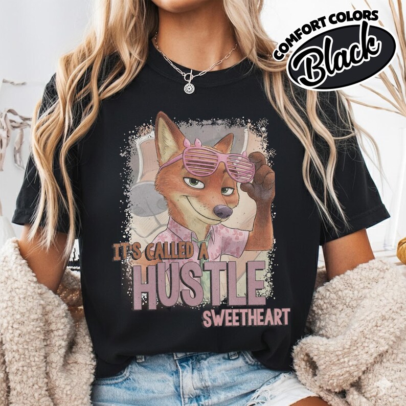 Puede incluir: Una camiseta negra con el gr&aacute;fico de un zorro de dibujos animados con gafas de sol de persiana rosas y una camisa estampada. El texto dice IT'S CALLED A HUSTLE SWEETHEART en una fuente rosa desgastada. Se ve una etiqueta Comfort Colors Black.
