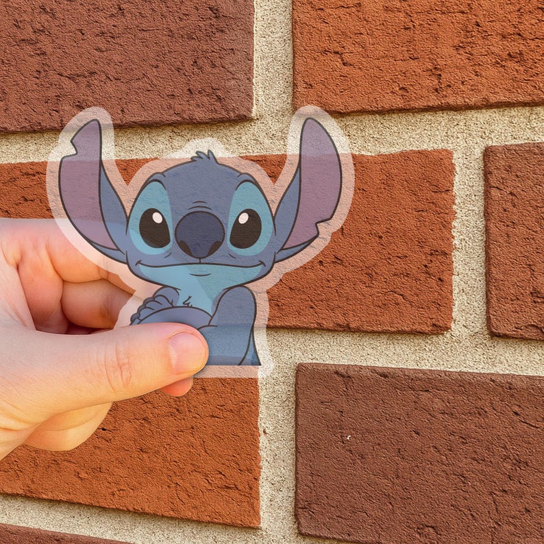 Może przedstawiać: Przezroczysta naklejka przedstawiająca postać Stitcha z filmu Disneya Lilo & Stitch. Stitch jest niebieski z dużymi uszami i przyjaznym wyrazem twarzy. Naklejka jest w stylu kresk&oacute;wkowym. Tło to czerwona ceglana ściana.