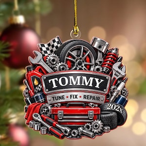 May include: A circular hanging ornament featuring automotive tools and parts including a tire, wrench, piston, and red toolbox. A central banner displays the name TOMMY with the text TUNE FIX REPAIR and 202x. The design includes a checkered flag.