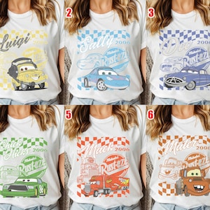 May include: White t-shirts featuring various cartoon car designs with names like "Luigi," "Sally," "Doc," "Chick Hicks," "Mack," and "Mater." Each design includes the year "2006" and the word "Rustez" in a circular emblem, with a checkered background.