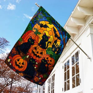 May include: A Halloween-themed flag featuring black cats with green eyes, jack-o'-lanterns, bats, and a haunted house against a stained-glass style background of orange, yellow, and blue. The flag is displayed outdoors, attached to a white house.