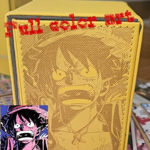 May include: Yellow card storage box with a detailed illustration of a character. The box has a textured surface and the words "full color art" are printed on the top. A smaller image of the character is in the bottom left corner.