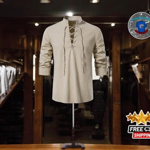 May include: A beige long-sleeve shirt with a lace-up neckline, displayed on a mannequin. The shirt has a mandarin collar and rolled-up sleeves. The background shows a clothing store with racks of clothing.