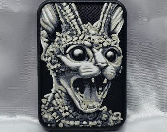 May include: A black rectangular phone case featuring a detailed, 3D-printed design of a screaming cat's face. The cat's face is rendered in shades of gray and white, with large, expressive eyes and an open mouth.