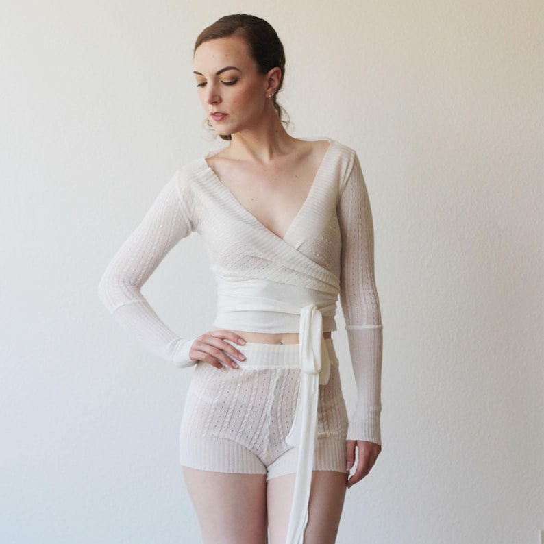 May include: White long-sleeved wrap top with a V-neck and a matching pair of shorts. The top is tied at the waist with a sash.