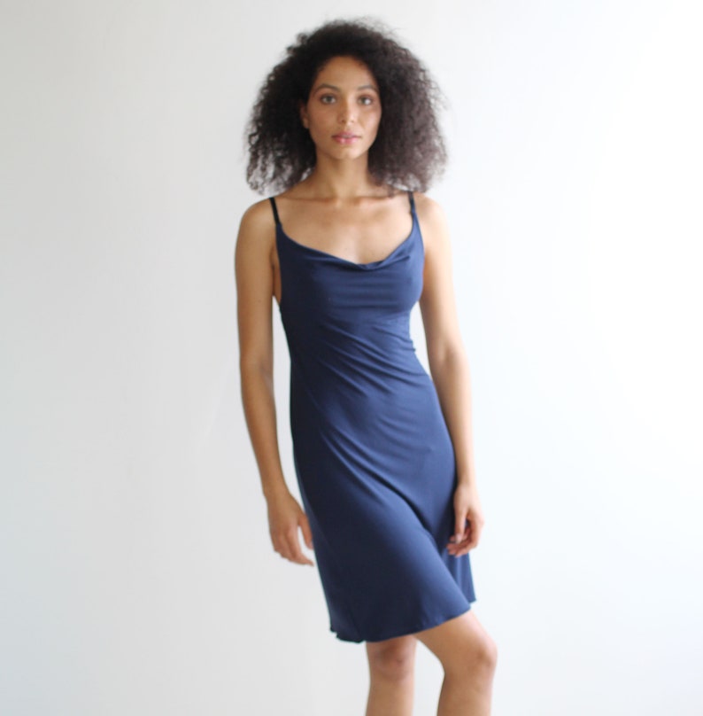 May include: A woman wearing a navy blue cowl neck slip dress.