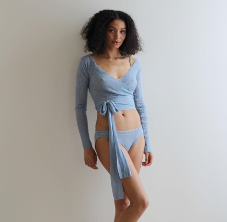 May include: A light blue wrap top with long sleeves and a tie at the waist. The top is made of a soft, stretchy fabric and is worn with matching light blue underwear.