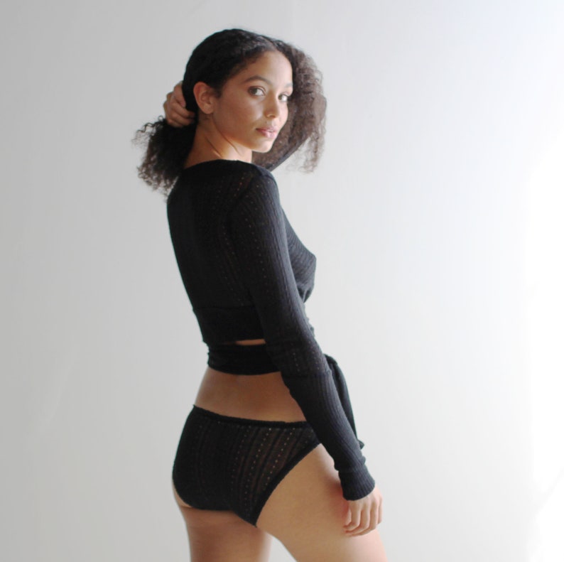 May include: A black long-sleeved top with a wrap design and a black lace-like pattern. The top is worn with black underwear that has a similar lace-like pattern.
