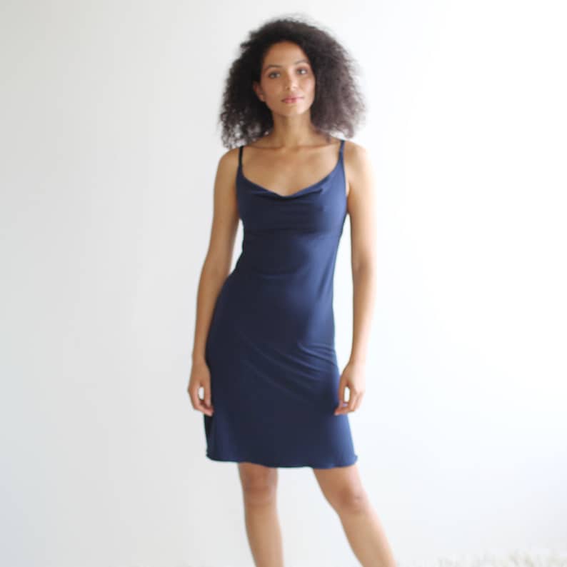 May include: A woman wearing a navy blue cowl neck slip dress.