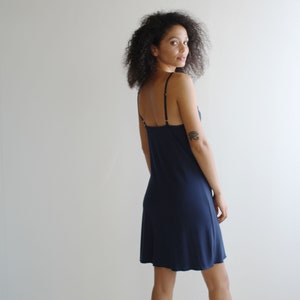 May include: A navy blue slip dress with thin straps. The dress has a straight silhouette and falls to the mid-thigh.