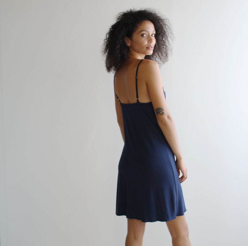 May include: A navy blue slip dress with thin straps. The dress has a straight silhouette and falls to the mid-thigh.