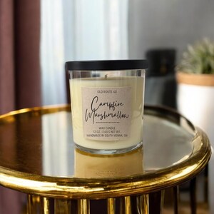 May include: A glass candle jar with a black lid and a brown paper label that reads "OLD ROUTE 40 Campfire Marshmallow WAX CANDLE 12 OZ. | 340 G NET WT. HANDMADE IN SOUTH VIENNA, OH".