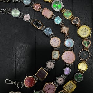 May include: A collection of various wristwatches with different colored faces and shapes, including round, square, and heart-shaped designs. The watches have metal bands and are arranged in a chain-like fashion. Some watches have Arabic numerals.
