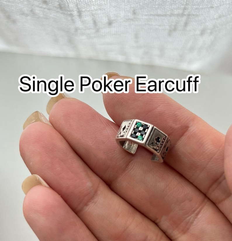 Puede incluir: Un earcuff de p&oacute;quer plateado &uacute;nico con un dise&ntilde;o rectangular. El earcuff presenta s&iacute;mbolos de naipes y piedras preciosas verdes y negras. El texto "Single Poker Earcuff" se muestra encima del earcuff.