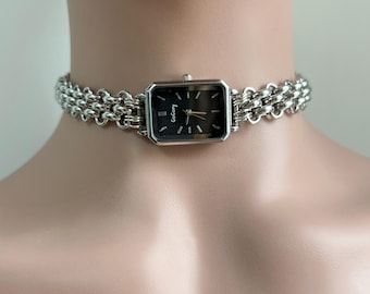 May include: A silver chain choker watch with a square black face and the word "Goofy" printed on it.