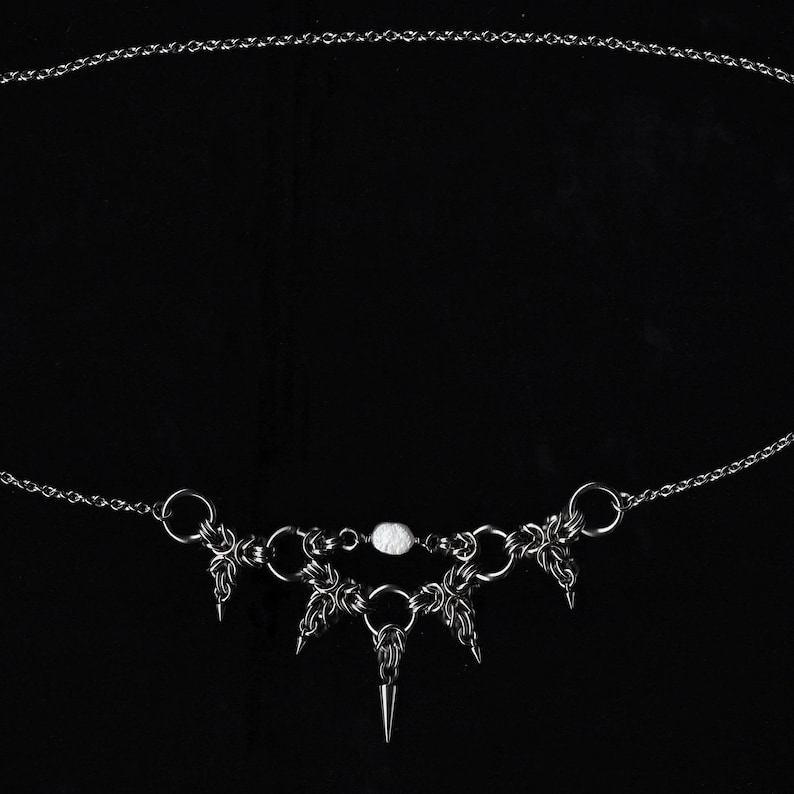 Op de afbeelding: Een zilveren ketting met een witte kraal en een hanger met vijf scherpe punten.
