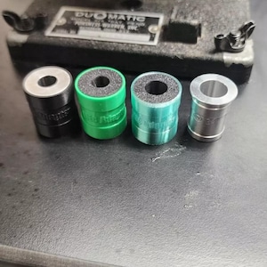 Pode incluir: Quatro anéis de metal de diferentes tamanhos, preto, verde, azul e prata, com um inserto de espuma preta. Os anéis estão sobre uma superfície preta.