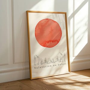 Puede incluir: Un póster vertical enmarcado que presenta un gran círculo rojo de acuarela texturizada en la parte superior. Debajo del círculo, una serie de dibujos de líneas negras representan una secuencia de posturas de yoga. El texto "Salutation au soleil" está impreso en negro en la parte inferior.