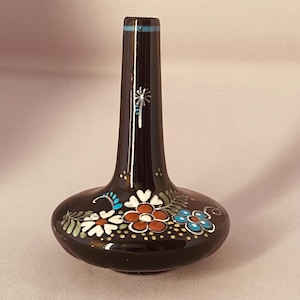 May include: A small, dark brown vase with a bulbous base and a slender neck. The vase is decorated with hand-painted floral designs in white, red, and blue, with green leaves and yellow dots. A turquoise band encircles the top.