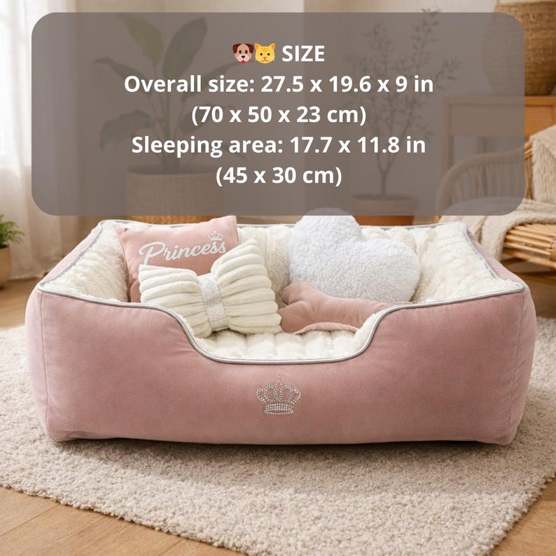 May include: A pink pet bed with a plush interior and decorative pillows. The bed has a crown emblem and is approximately 27.5 x 19.6 x 9 inches (70 x 50 x 23 cm) overall. The sleeping area is about 17.7 x 11.8 inches (45 x 30 cm).