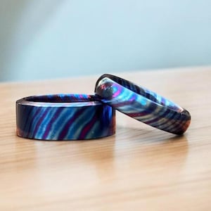 Könnte beinhalten: Zwei Ringe aus blauem, violettem und rotem gemustertem Metall. Die Ringe sind übereinander gestapelt.