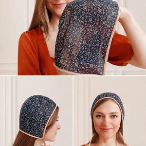 May include: A dark blue bonnet featuring a small-scale floral pattern in white and light blue. The head covering is finished with a solid light peach-colored trim along the edges and includes two matching thin fabric ties for securing under the chin.