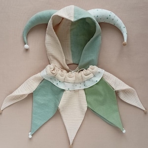 Puede incluir: Una capucha de buf&oacute;n caprichosa en colores pastel suaves. La capucha presenta una combinaci&oacute;n de telas verdes, beige y blancas, con un cuello con volantes y detalles puntiagudos. Tiene dos cuernos largos y curvos con peque&ntilde;os pompones en las puntas, para disfraz o juego.