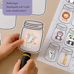 May include: A child's hand holds a torch, illuminating a paper cutout of an elephant inside a jar. The image includes other jar cutouts and a sheet with various animal illustrations inside jars. Text reads "So fortiger Spielspaß mit Licht zum ausdrucken!"