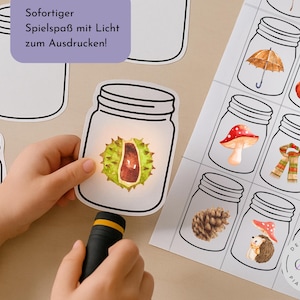 May include: A child's hand shines a light on a paper mason jar containing a chestnut. Other paper jars with autumn-themed illustrations are visible. Text on a purple background reads "Immediate fun with light to print!"