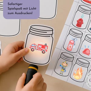 以下が含まれることがあります： 子供の手が、懐中電灯で照らされた赤い消防車のイラストが描かれた紙の瓶を持っています。他の瓶のイラストには、消火栓、消防士、火が含まれています。画像には「印刷する光でインスタントな楽しみ！」と書かれています。