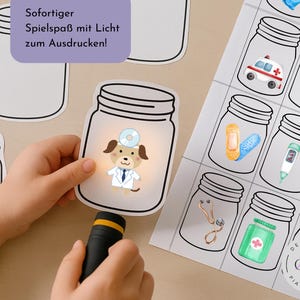 Op de afbeelding: Een kinderhand houdt een zaklamp vast die een cartoonhond-dokter in een glazen pot-uitsparing verlicht. Andere potuitsparingen en een vel met illustraties van medische potten zijn zichtbaar. De tekst in de afbeelding luidt "Sofortiger Spielspaß mit Licht zum Ausdrücken!"