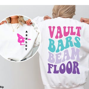 May include: White sweatshirt with the words "VAULT BARS BEAM FLOOR" in colorful retro font. The words are stacked vertically and each word is a different color. The sweatshirt has a pink gymnast silhouette on the front.