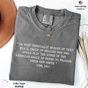 Könnte beinhalten: Ein graues T-Shirt mit einem weißen Zitat von Franklin Delano Roosevelt: "We must especially beware of that small group of selfish men who would clip the wings of the American eagle in order to feather their own nests." -FDR, 1941.