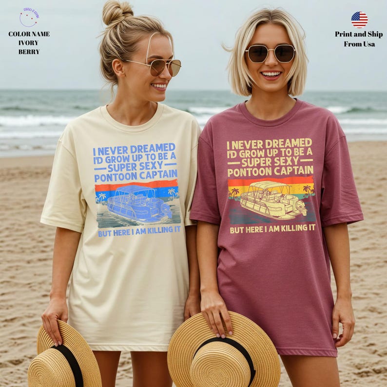 K&ouml;nnte beinhalten: Zwei &uuml;bergro&szlig;e T-Shirts, eines in Elfenbein und eines in Beere, mit dem Text "I NEVER DREAMED I'D GROW UP TO BE A - SUPER SEXY - PONTOON CAPTAIN." Jedes Shirt zeigt eine Pontonboot-Grafik und den Satz "BUT HERE I AM KILLING IT."