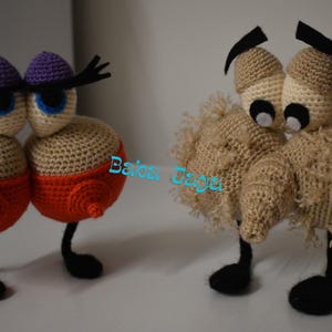 Puede incluir: Dos criaturas de ganchillo hechas a mano. Un par tiene cuerpos color canela con fondos naranjas, ojos azules y sombreros morados. El otro par tiene cuerpos color canela con ojos negros y detalles negros. Ambos tienen piernas y pies negros.